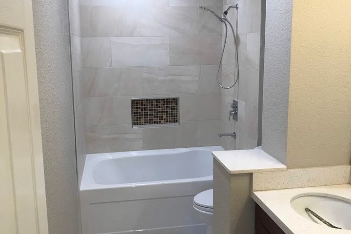 Bathroom with gray tiled tub surround, shower fixtures, and vanity